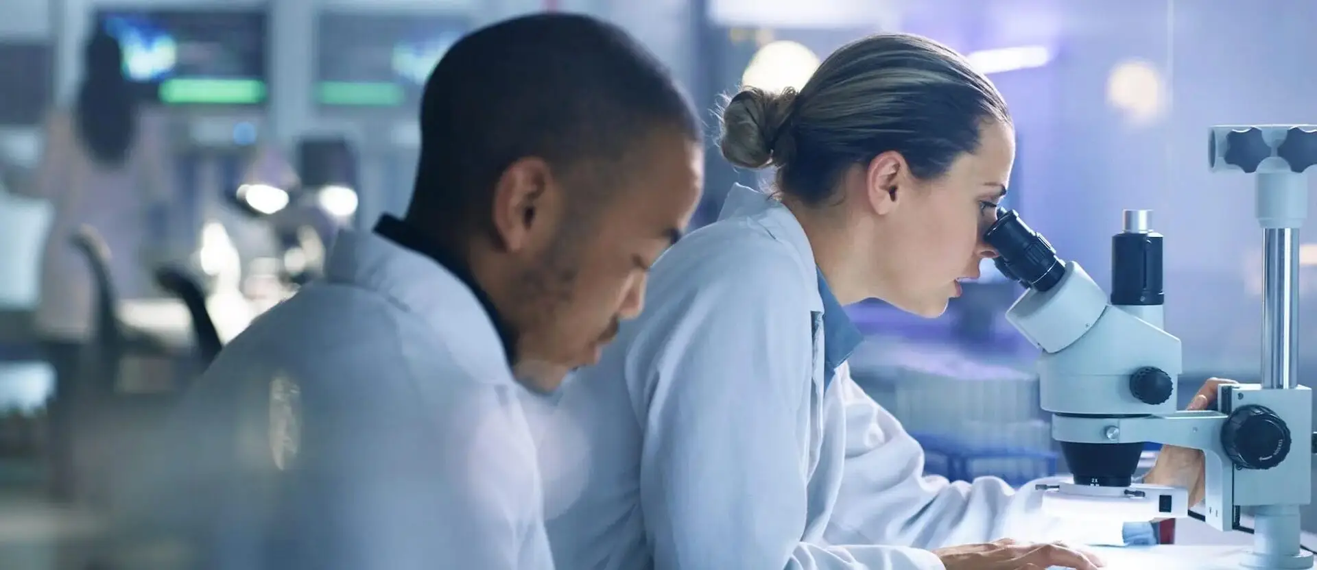 Image of two scientists in a lab with one of them looking in a microsope.